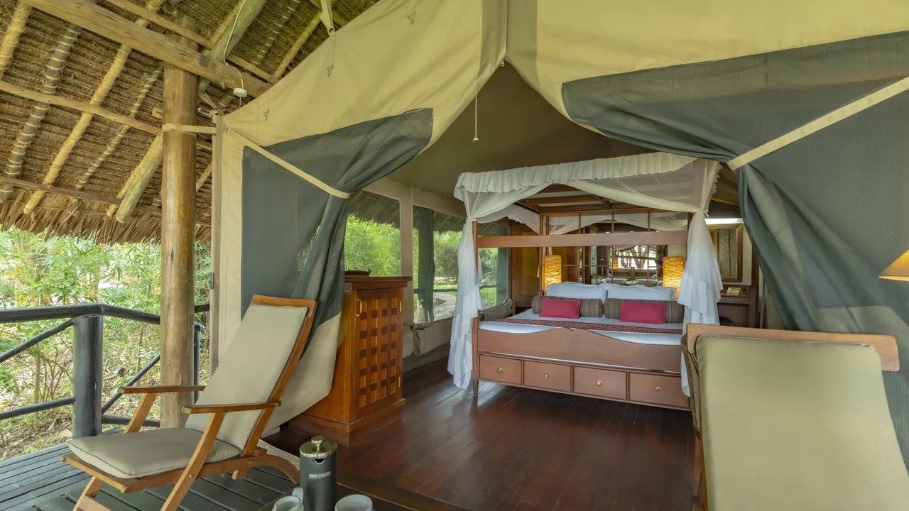 View from the deck into a tent at Samburu Intrepids, with a canopy bed, pink cushions and wooden chest