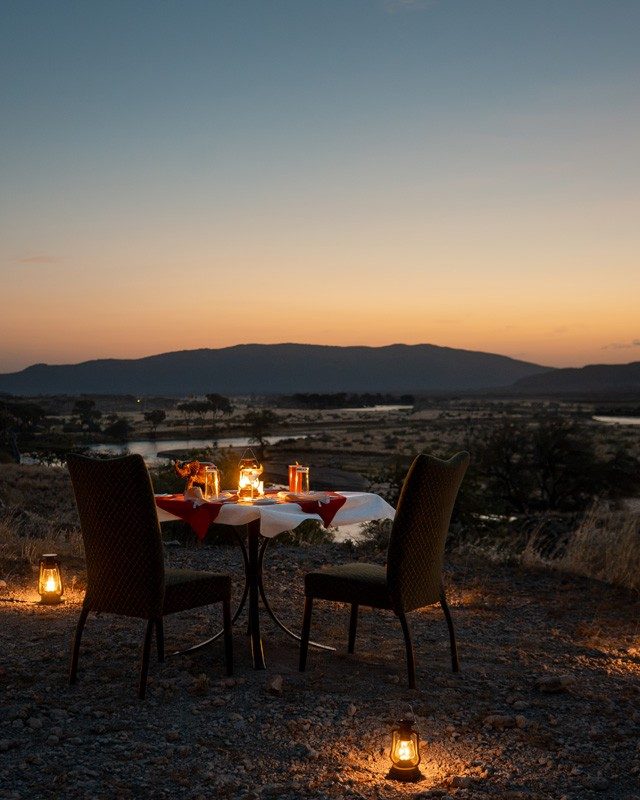 Dinner table set with lanterns outdoors at dusk near Samburu Simba Lodge, with hills fading on the horizon