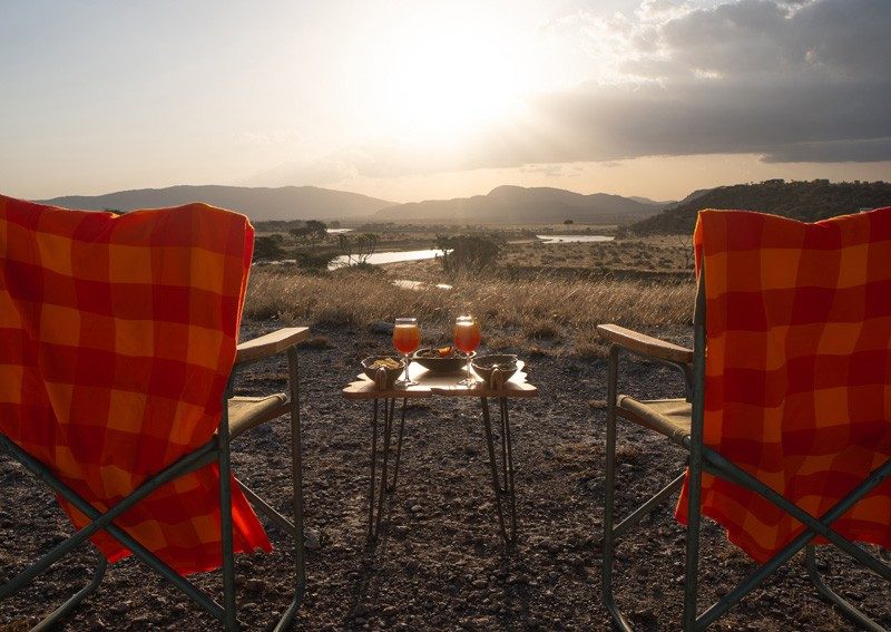 Two checked safari chairs and drinks set out for a sundowner on a rise near Samburu Simba Lodge, facing the low sun