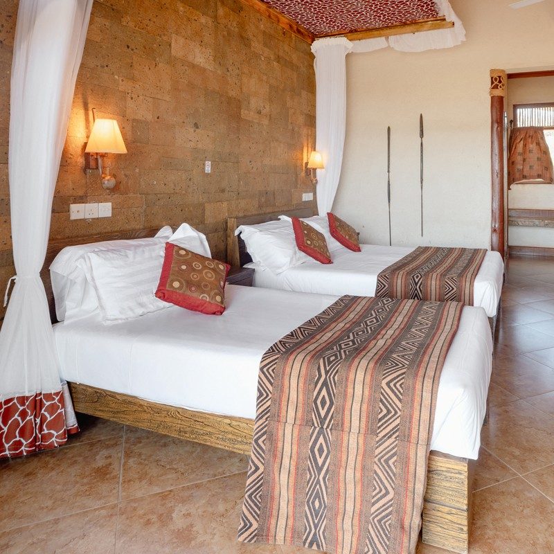 Twin room at Samburu Simba Lodge with stone walls, white netting and beds dressed in striped throws