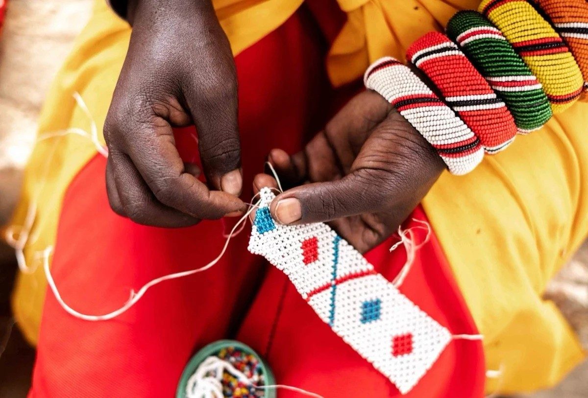 Close view of hands threading a colourful bead pattern, with beaded bracelets on the wrists, at Sarara Camp