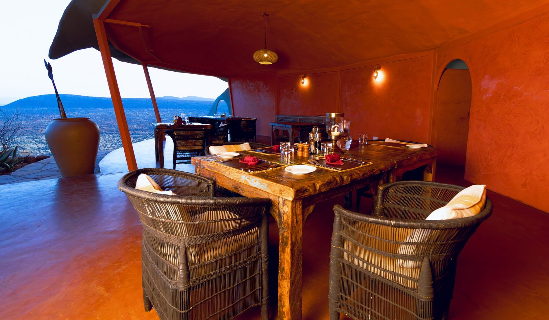 Wooden dining table with woven chairs at Saruni Samburu, open on one side to the hills