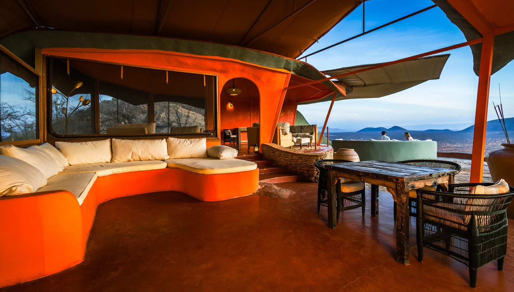 Curved built-in sofa and dining tables under an orange canopy in the open main lounge at Saruni Samburu