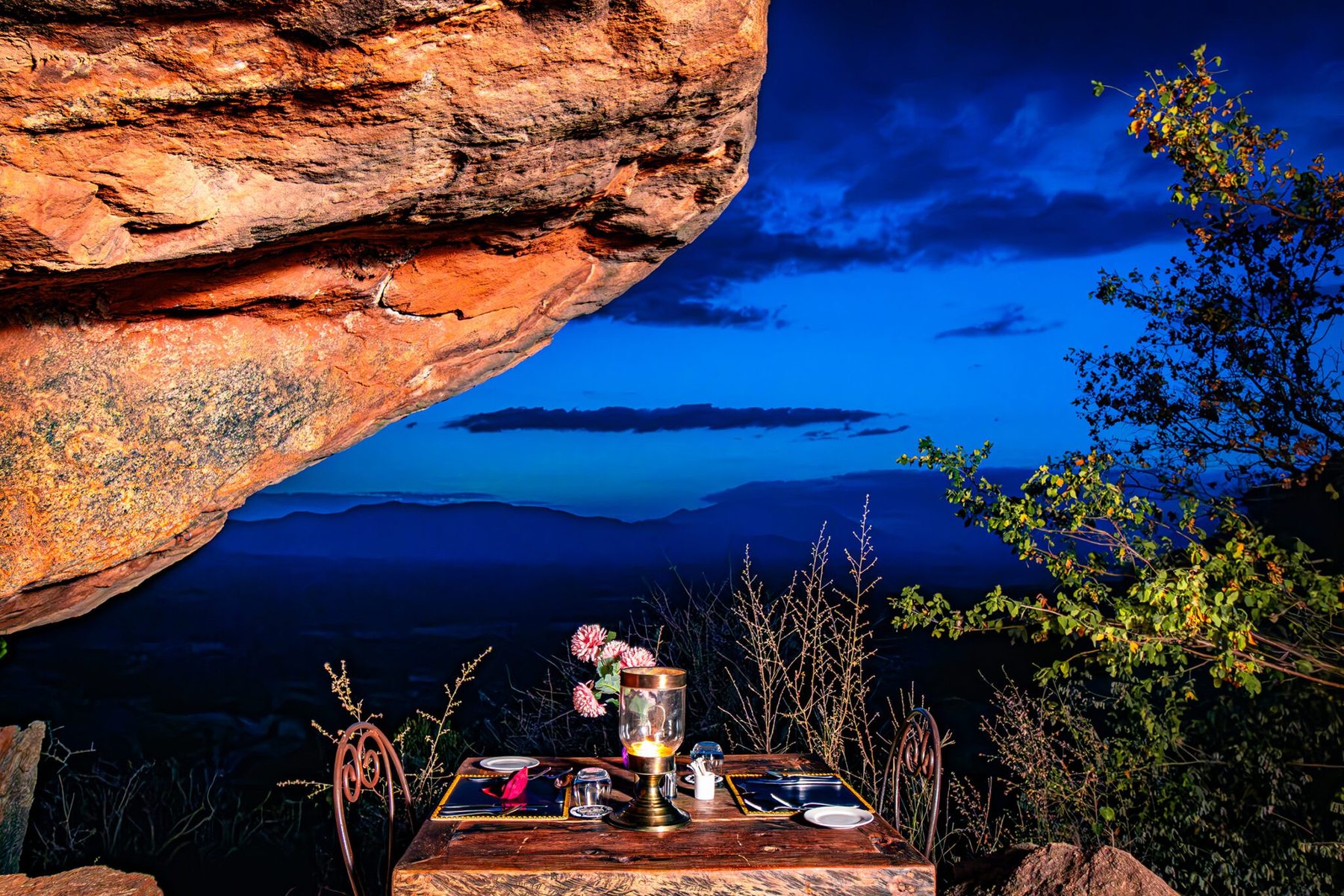 Candlelit table beneath a rock overhang at Saruni Samburu, looking out over the plains at dusk