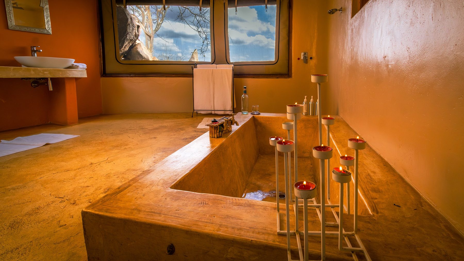 Sunken stone bathtub lined with candles beneath a window in a villa bathroom at Saruni Samburu
