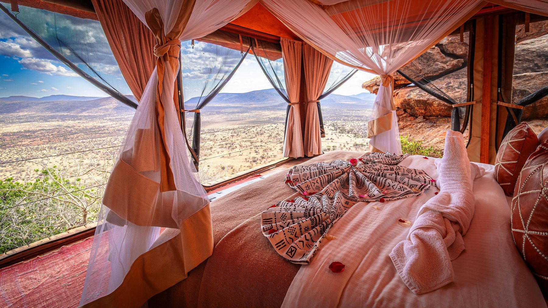 Bed under draped netting at Saruni Samburu, with wide windows looking out over dry plains and hills
