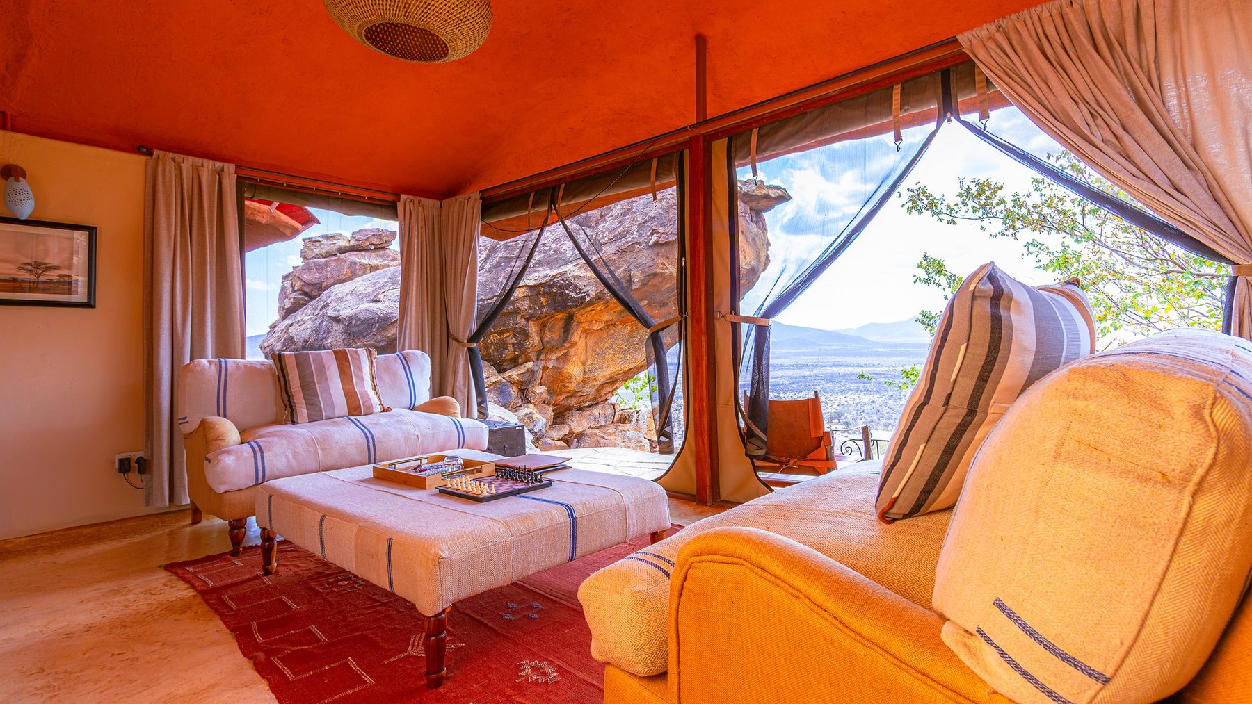 Sofas and an upholstered ottoman in a villa at Saruni Samburu, open to boulders and the view beyond