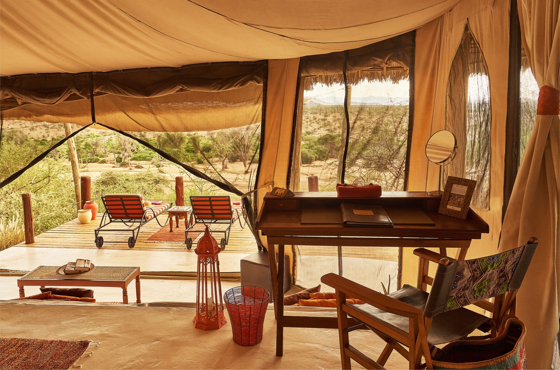Writing desk and chairs inside a tented room at Sasaab, opening onto a deck with red loungers and bush beyond