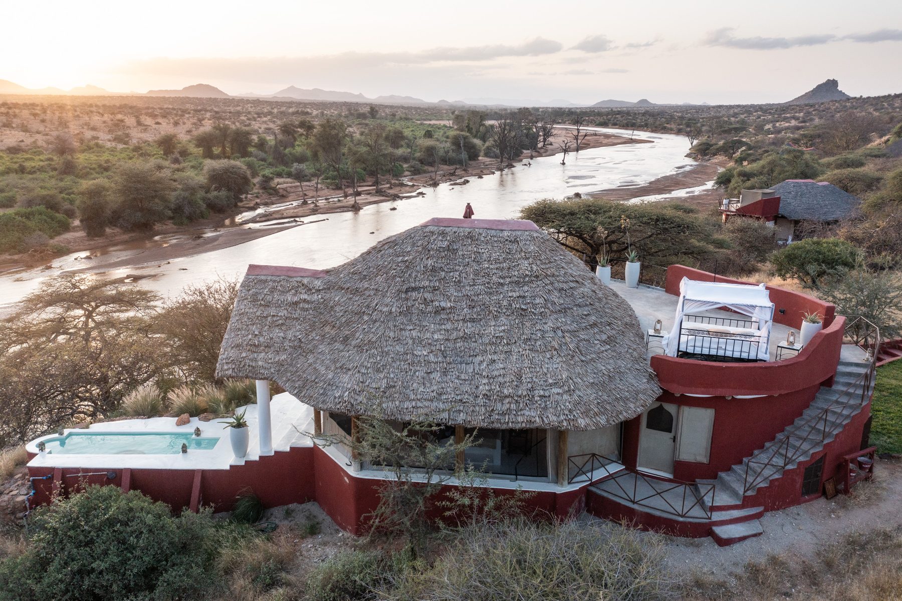 Thatched room with red walls and a deck at Sasaab, set on a ridge above the river at dusk