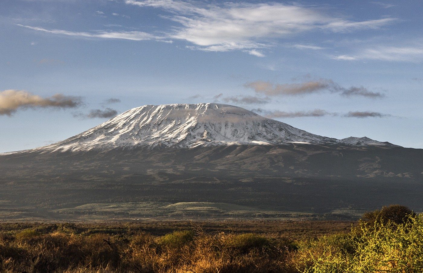 Snow-capped summit of Kilimanjaro above a band of cloud and bush, seen from near Satao Elerai
