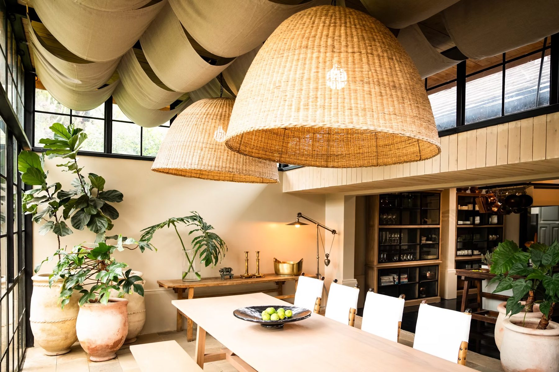 Light-filled dining room at Segera Retreat with a long wooden table, large woven pendant lamps and potted plants