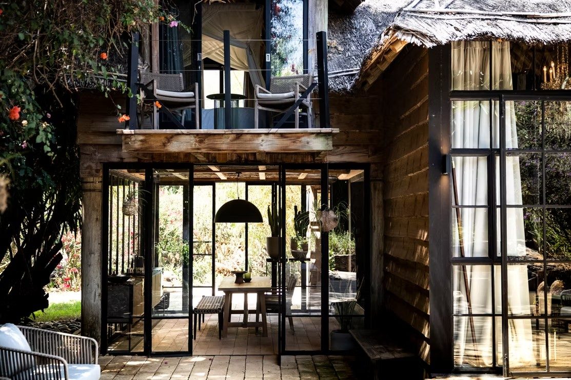 Glass-walled pavilion with dark steel frames and a thatched roof beside a garden path at Segera Retreat