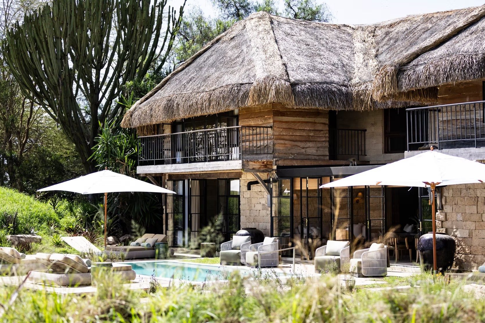 Two-storey stone and thatch house at Segera Retreat with white umbrellas and loungers around a garden pool