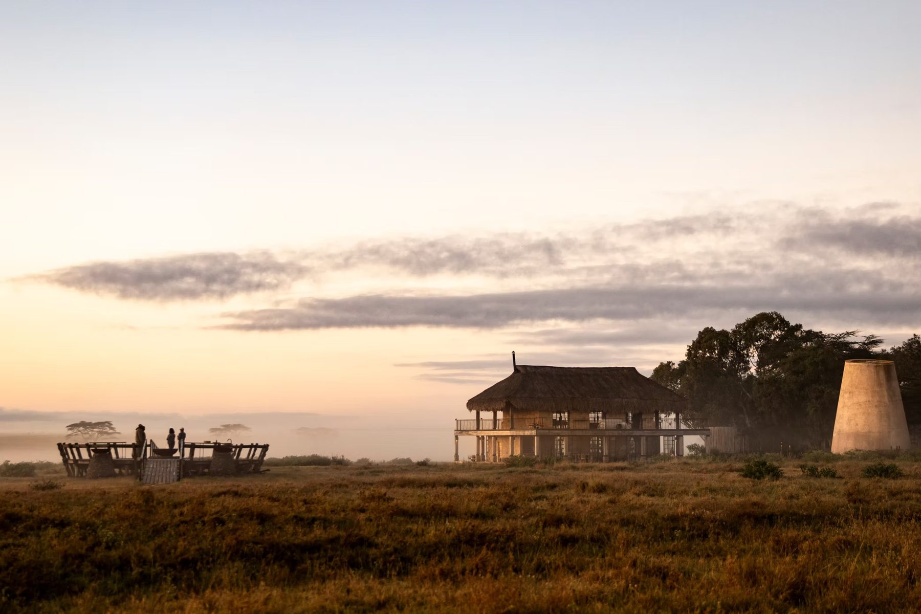 Raised viewing deck and thatched buildings on open grassland under a pale sunset sky at Segera Retreat
