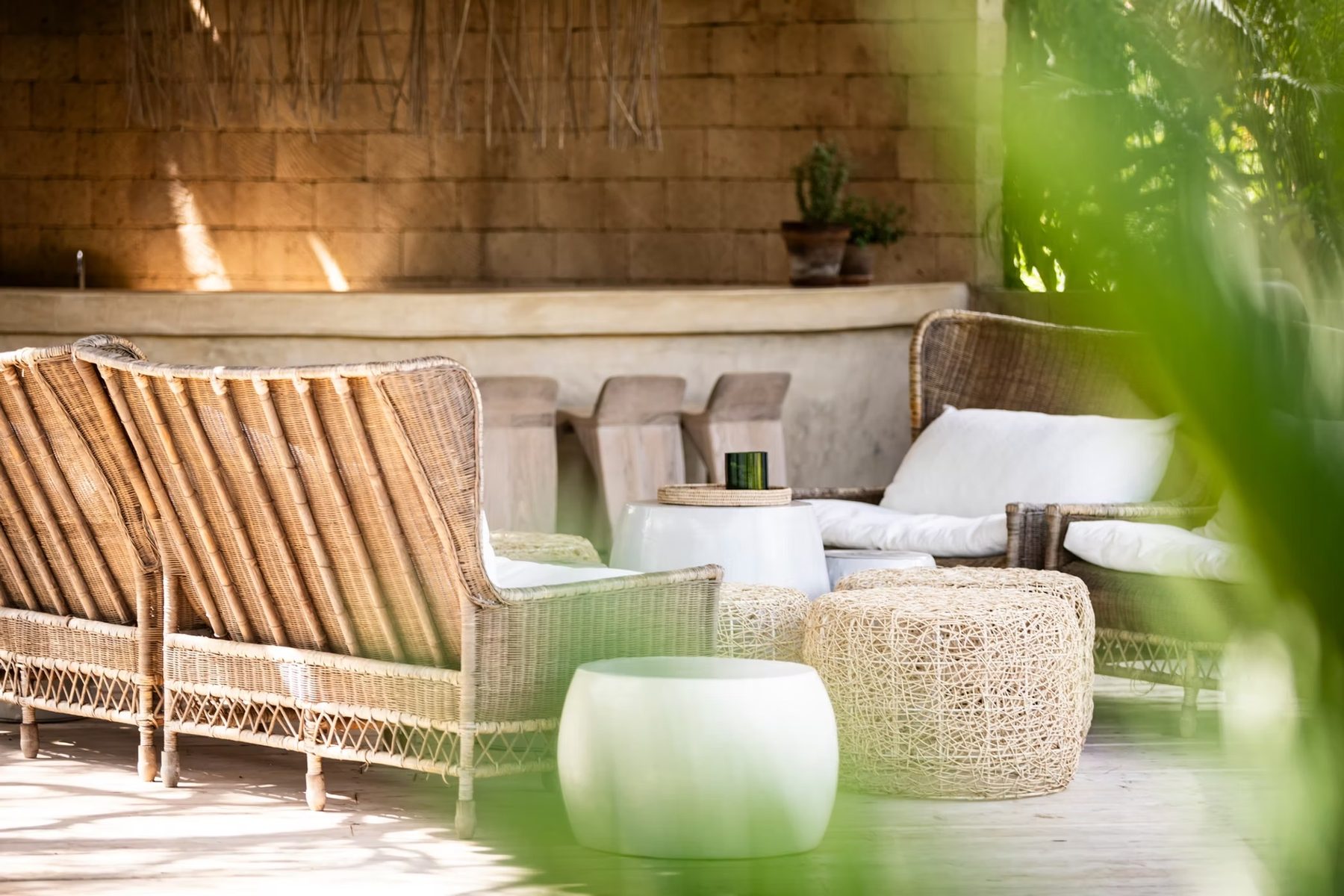 Woven armchairs, a low sofa and wicker stools on a sunlit terrace beneath a thatched wall at Segera Retreat