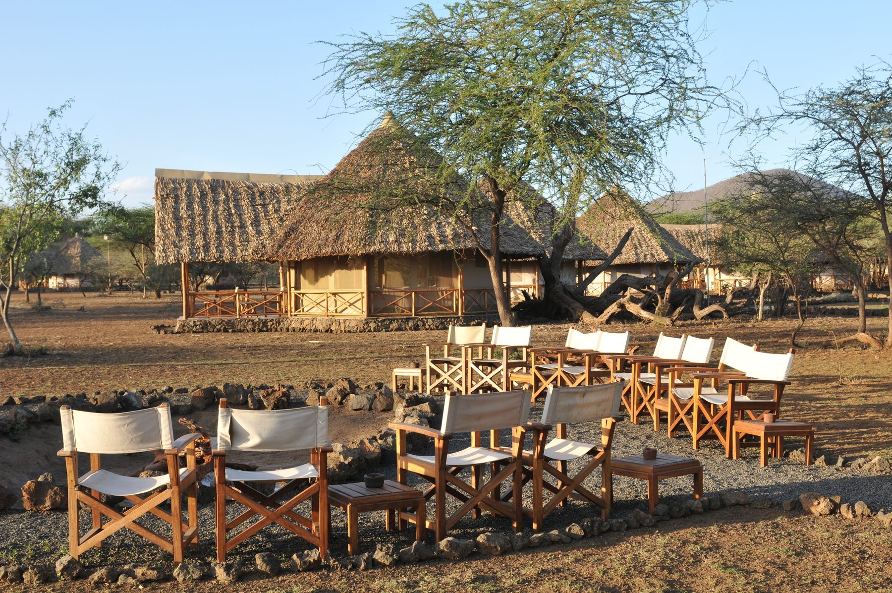 Circle of director’s chairs around a fire pit in front of thatched buildings at Severin Safari Camp