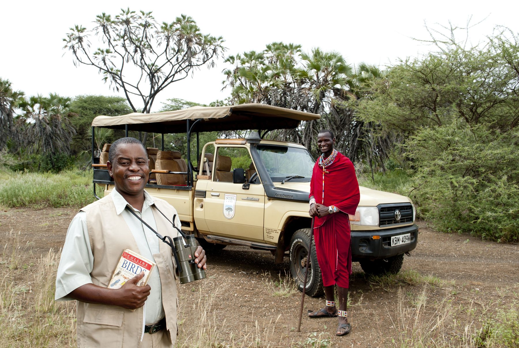 Guide and Maasai tracker beside a game drive vehicle from Severin Safari Camp in green bush