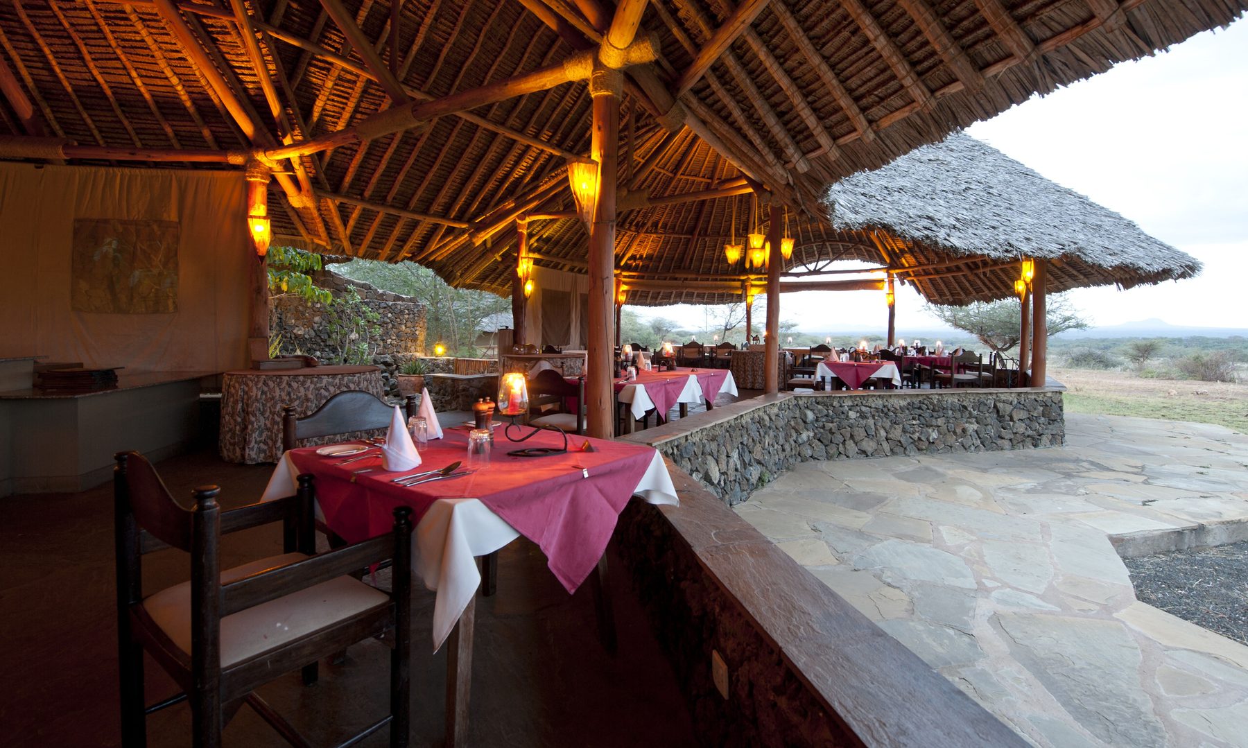 Open thatched restaurant at Severin Safari Camp with candlelit tables and red tablecloths