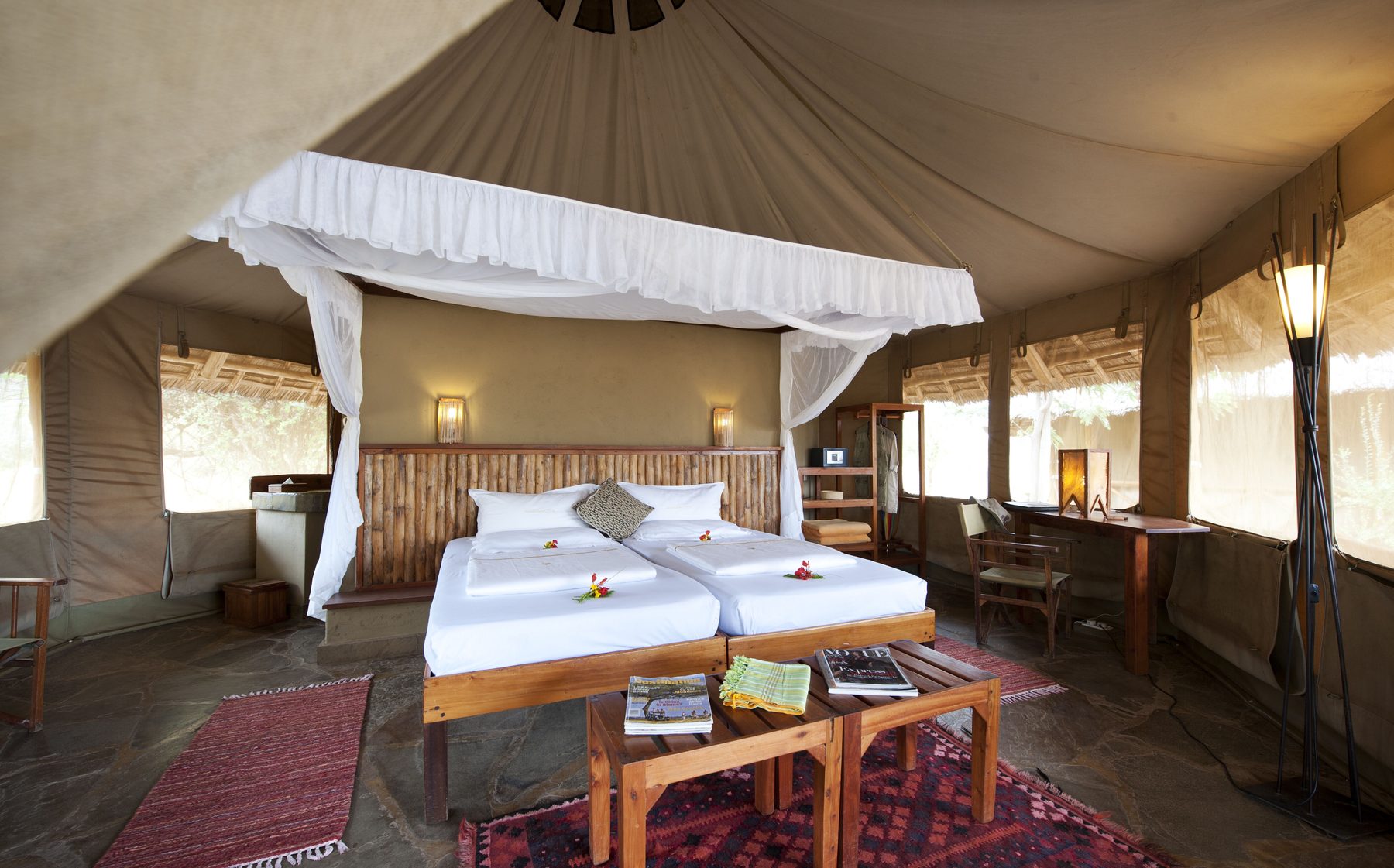 Twin beds under a white net canopy in a spacious tent with rugs and a writing desk at Severin Safari Camp