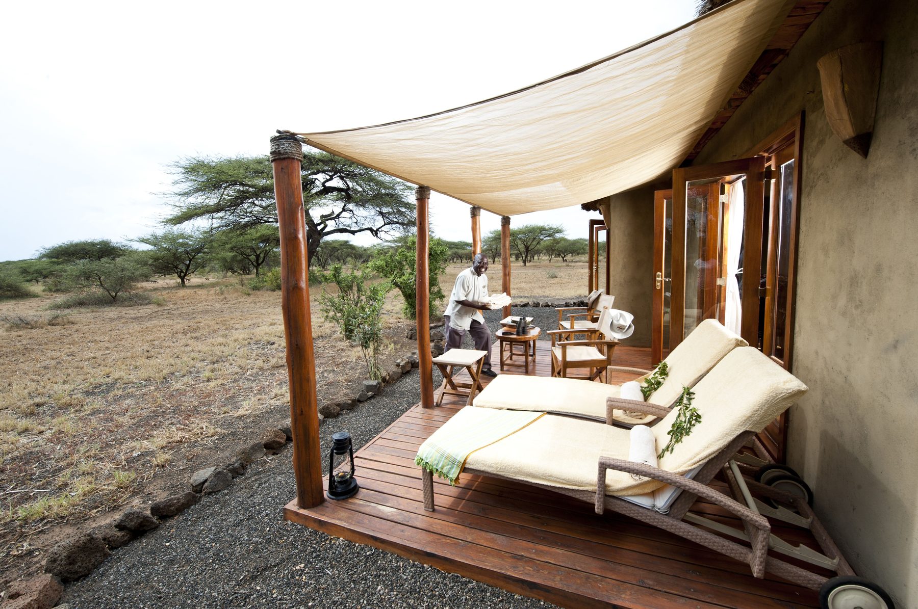 Loungers on a shaded wooden veranda outside a tent at Severin Safari Camp, looking out over dry bush