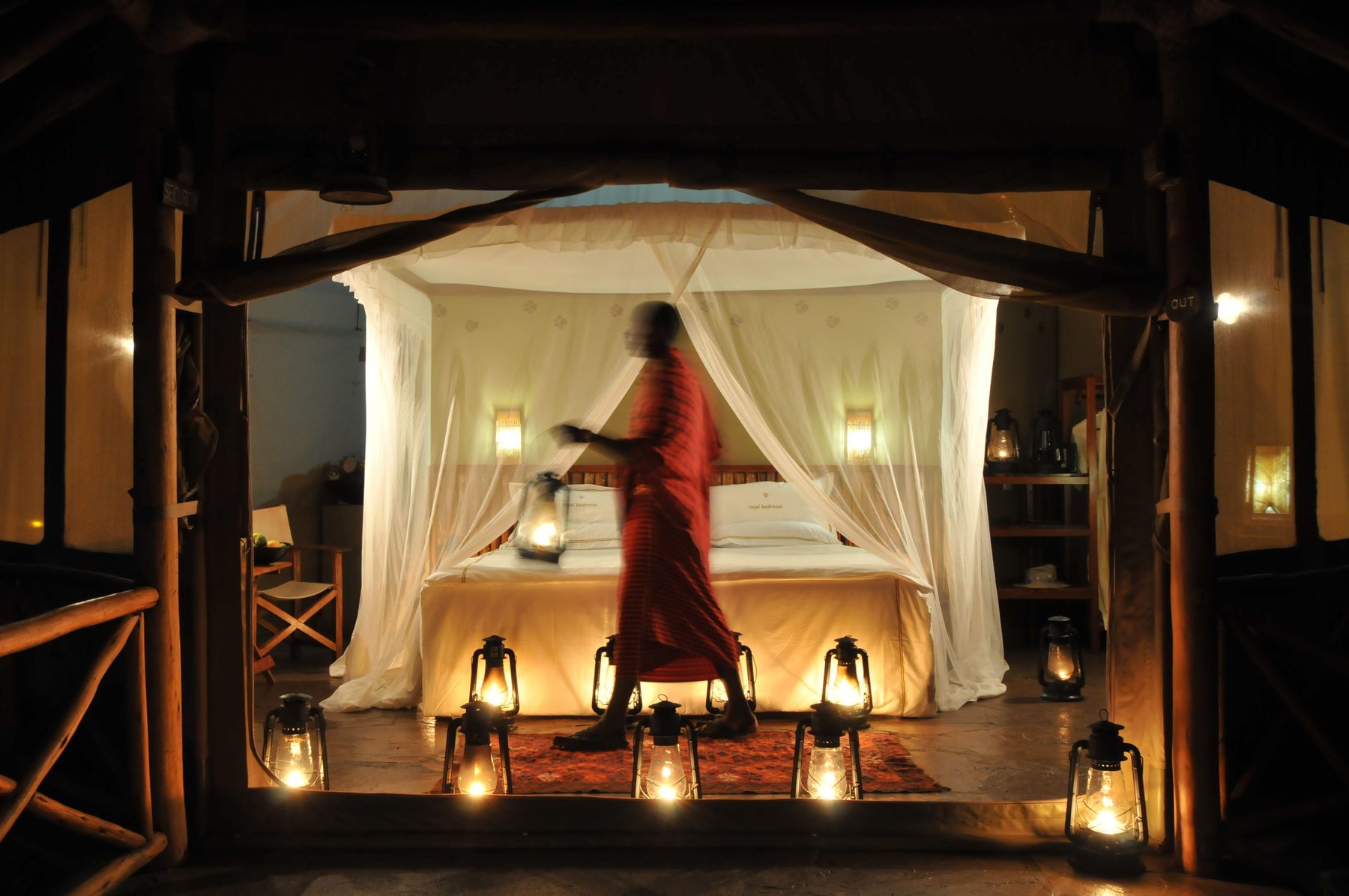 Maasai host lighting lanterns beside a netted bed at the open door of a tent at Severin Safari Camp at night