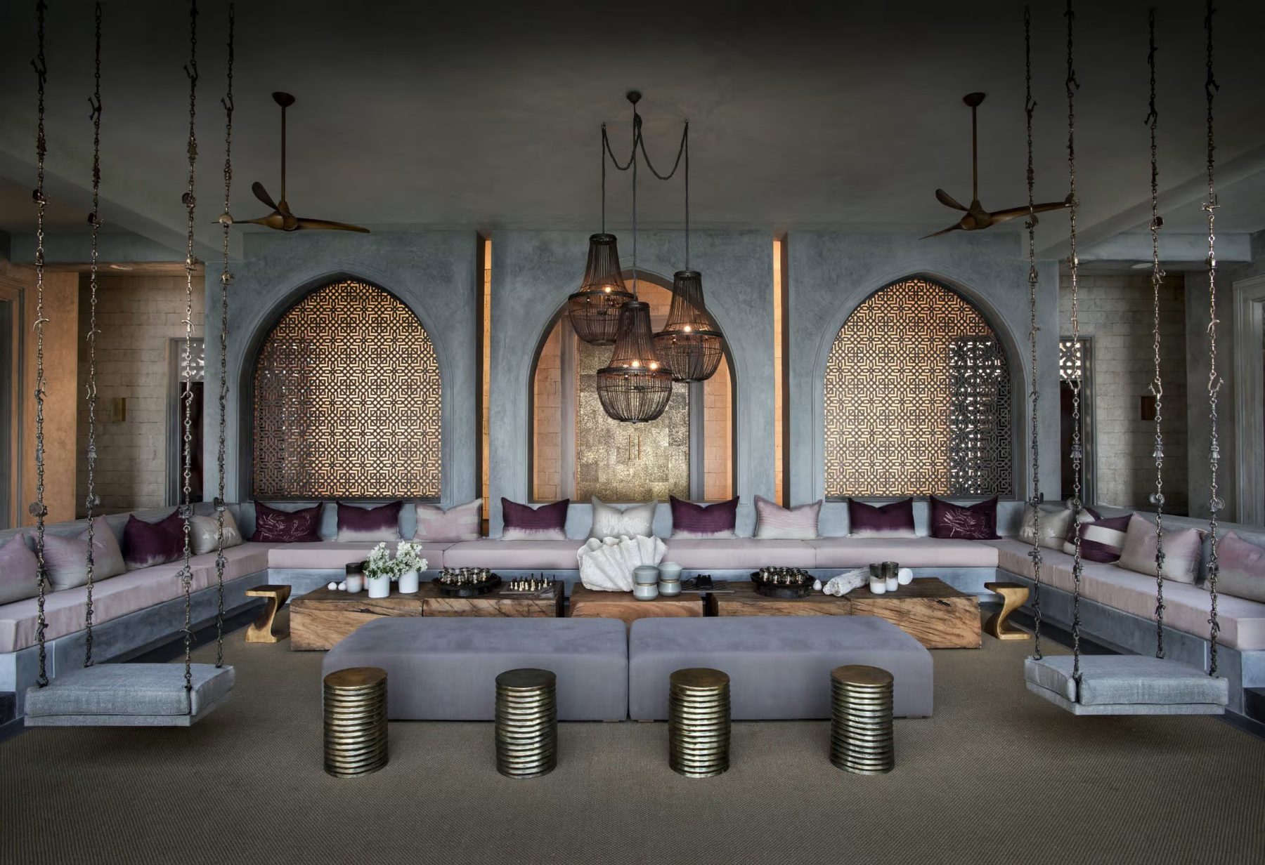 Sunken lounge with grey sofas below carved arches and hanging lanterns at Sirai House