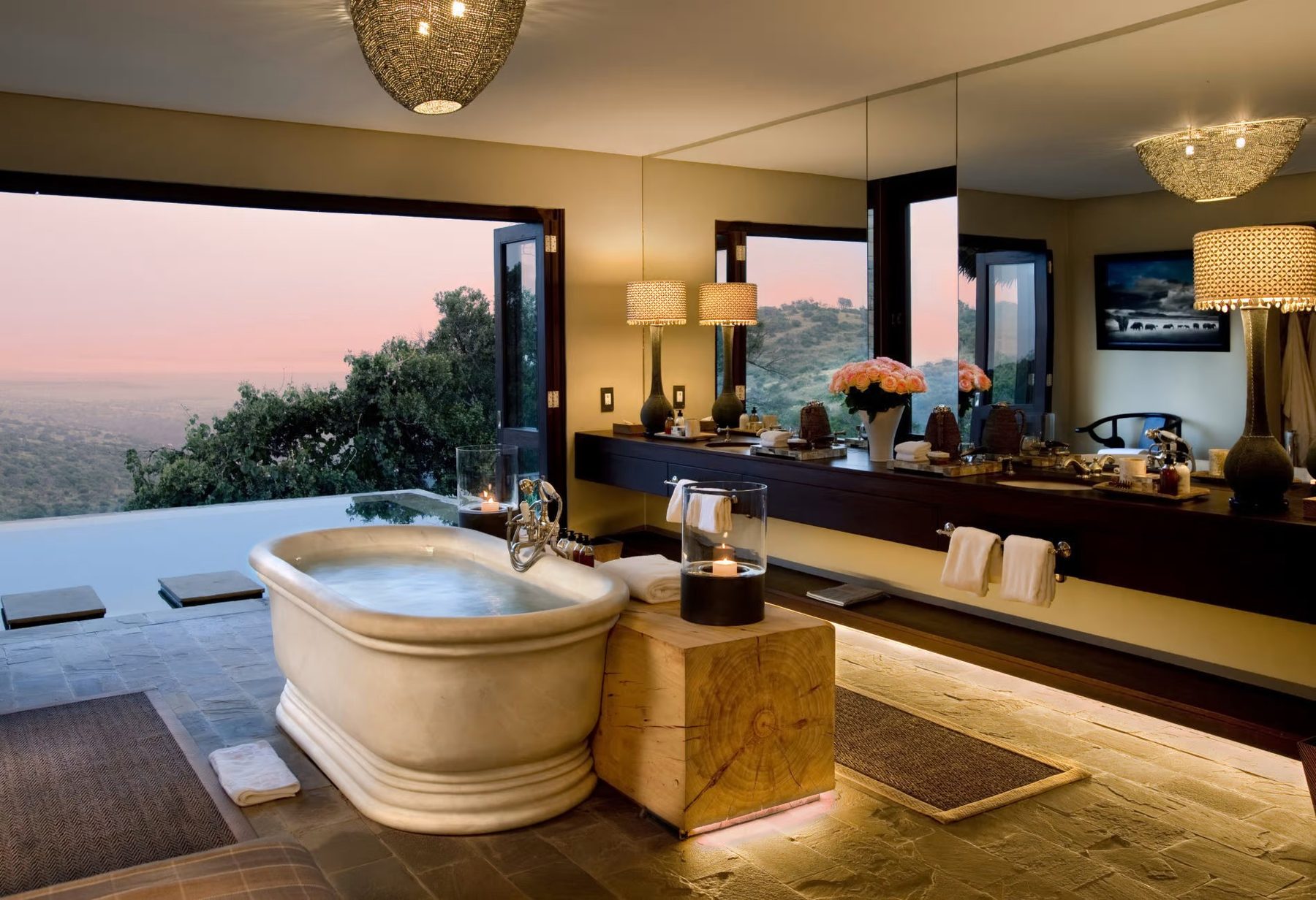 Freestanding bathtub with candles in a bathroom at Sirai House, wide windows looking out to hills at dusk