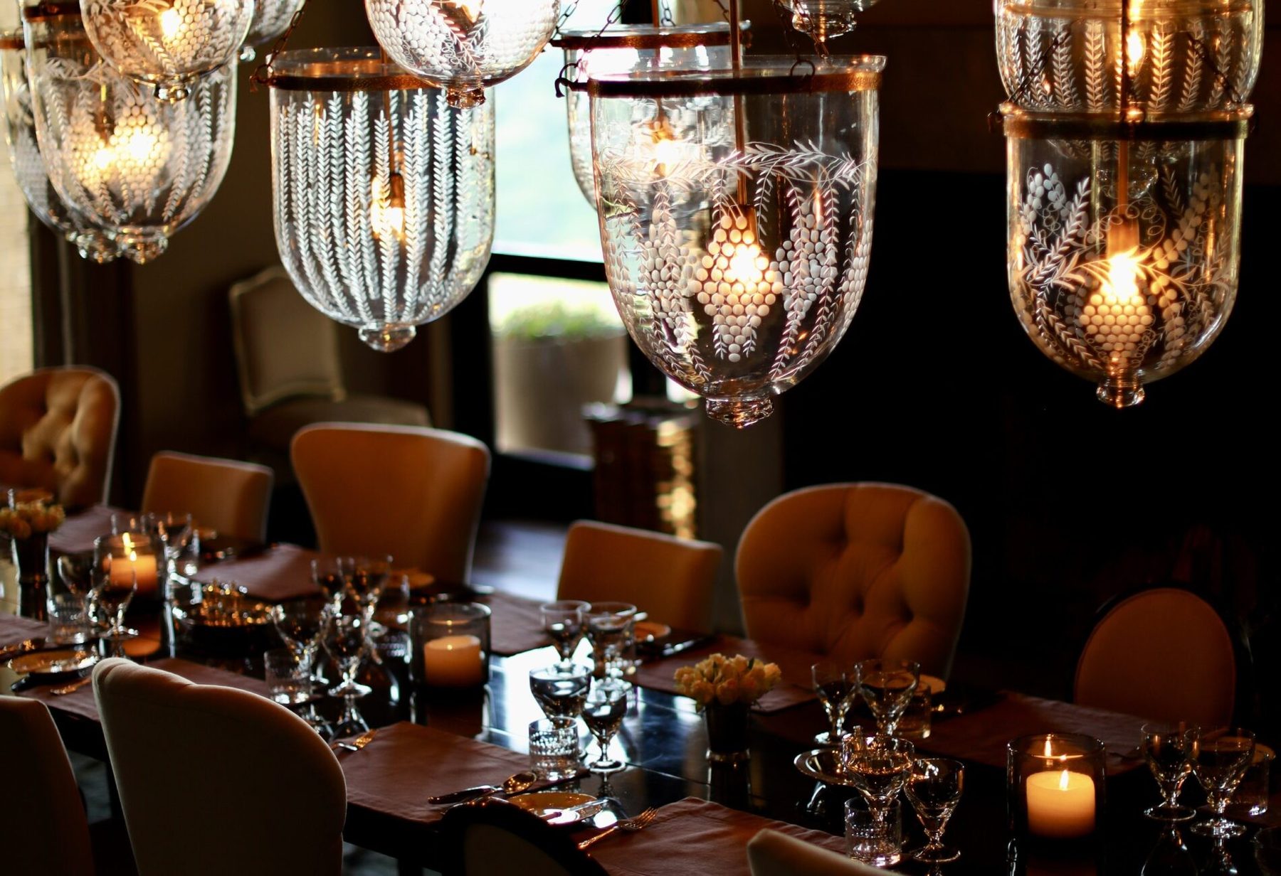 Dining table set with candles and glasses beneath glass lanterns and leather chairs at Sirai House