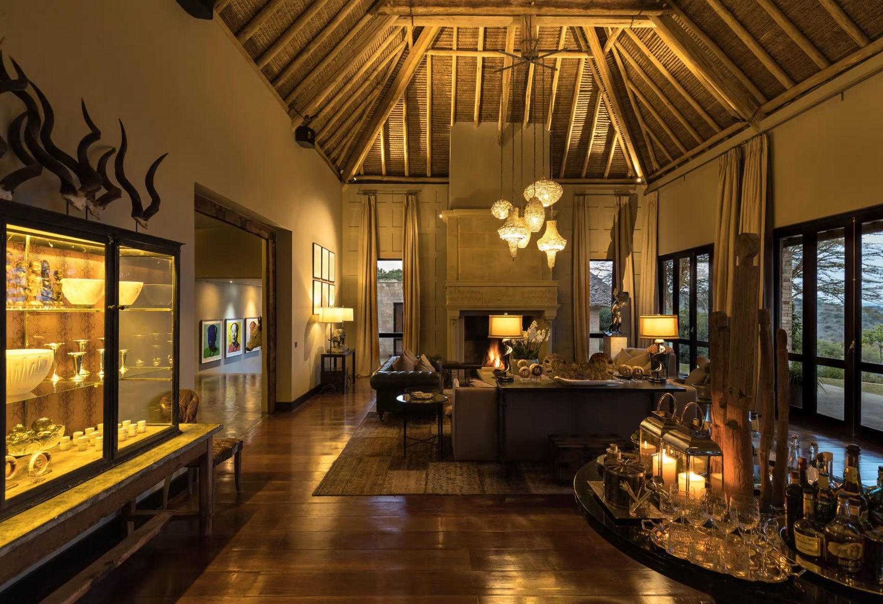 Double-height room at Sirai House under a timber roof, with lit display cabinets, sofas and pendant lights
