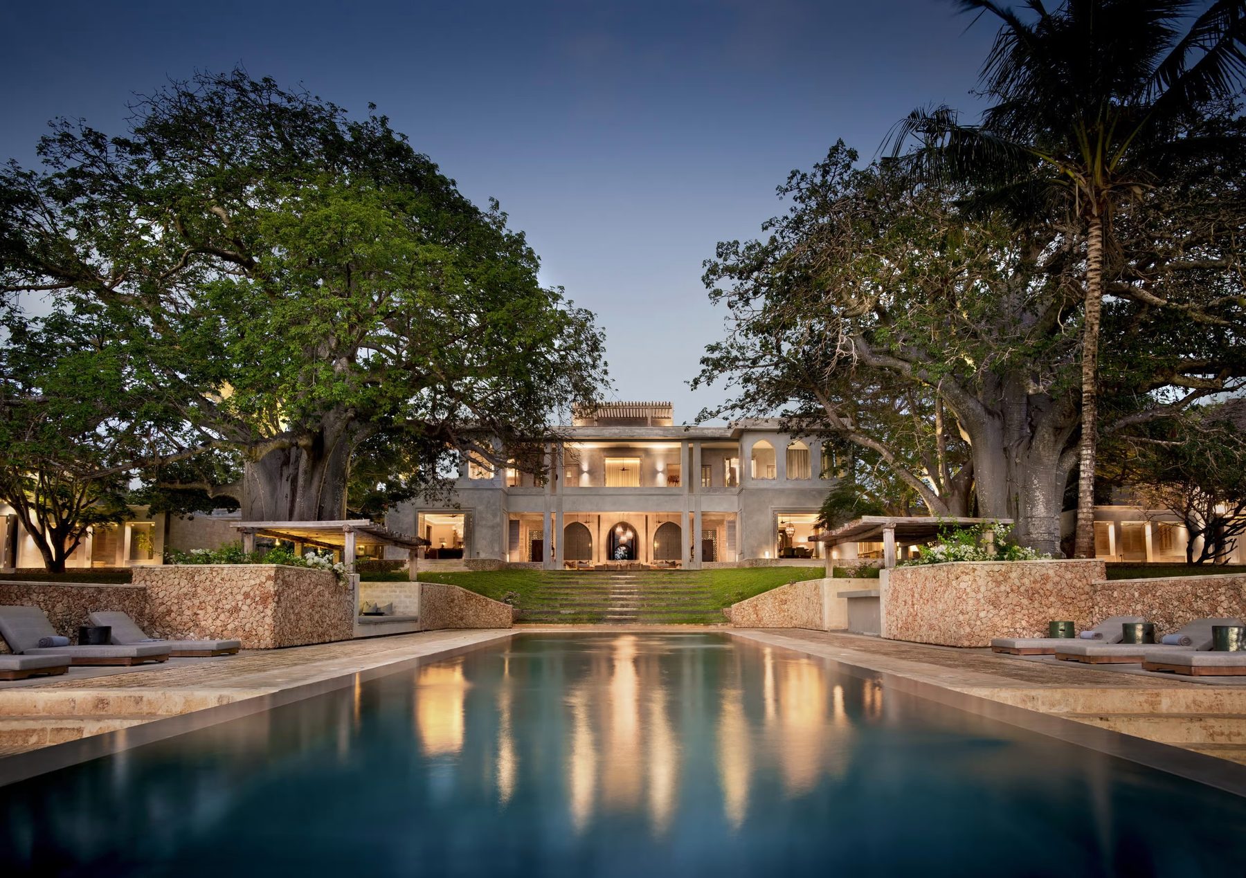 Long reflecting pool leading to Sirai House lit up at dusk among tall trees