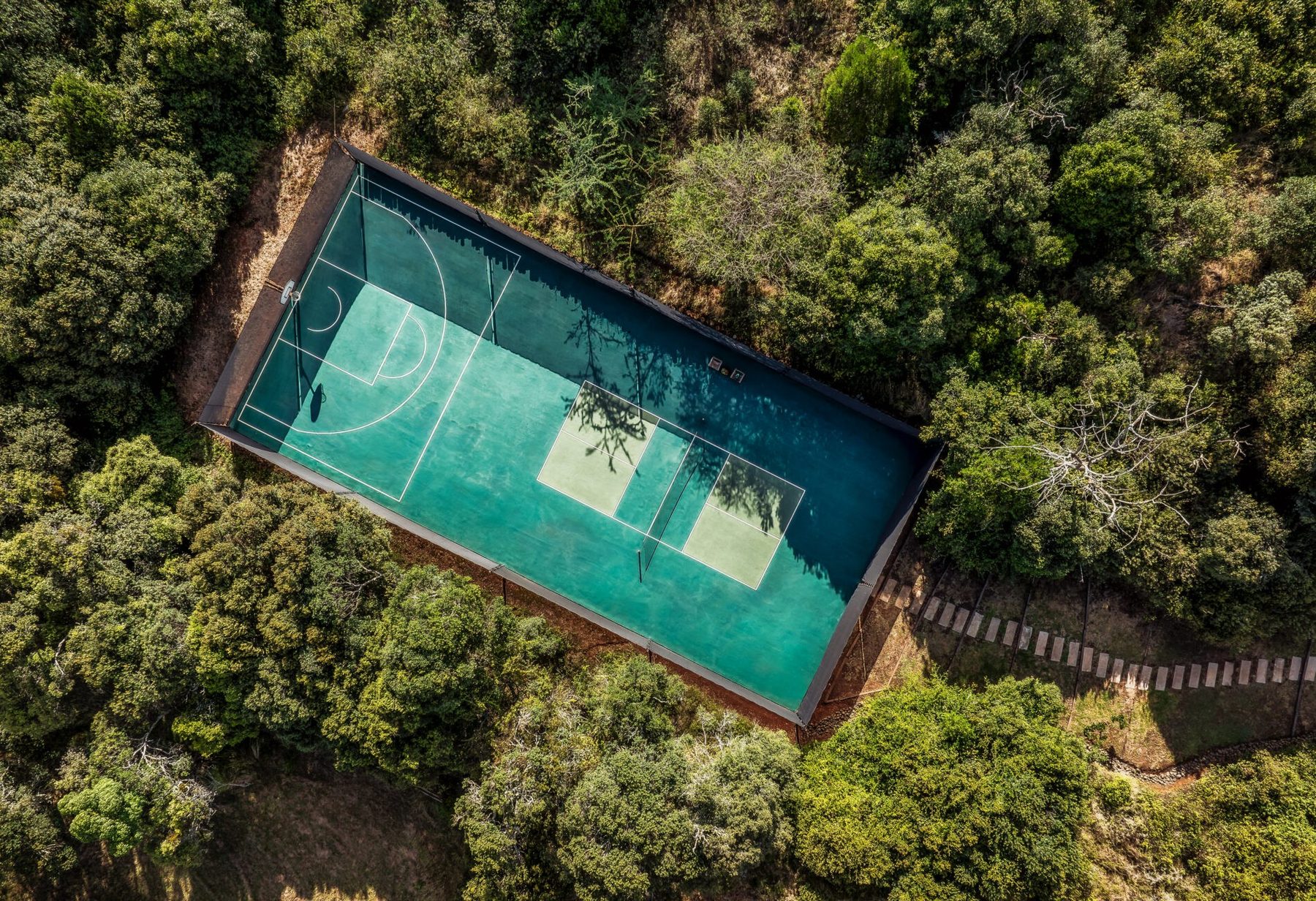 Aerial view of a tennis court set into thick green woodland at Sirai House