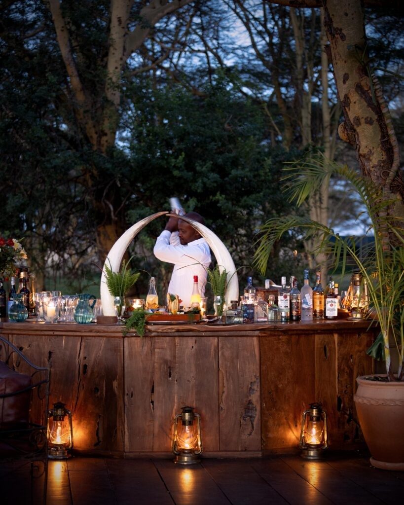 Wooden bar lit by lanterns among trees at Sirikoi, with a barman behind the counter