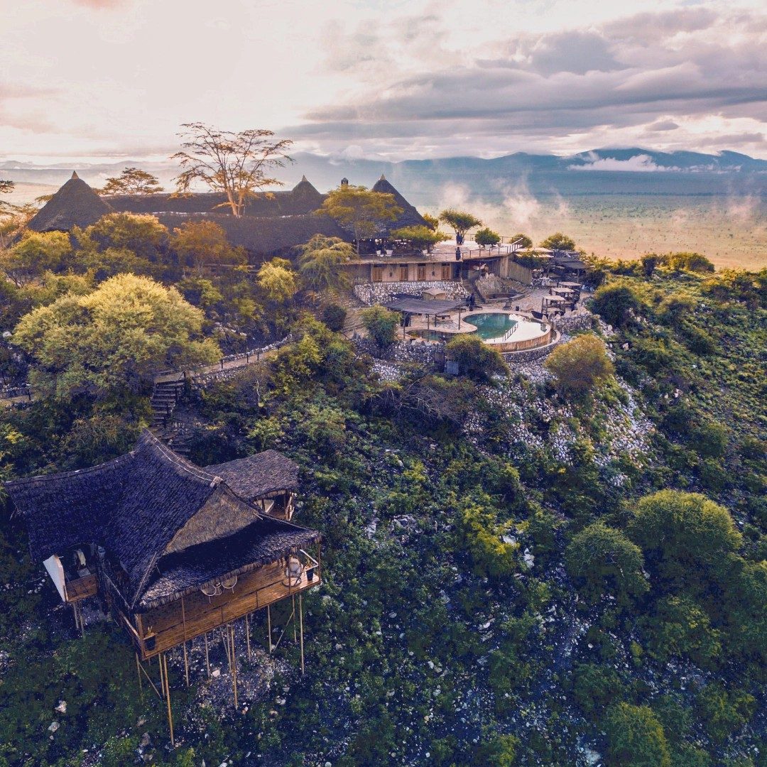 Aerial view of the thatched buildings of Soroi Cheetah Tented Camp spread across a wooded rise at dusk