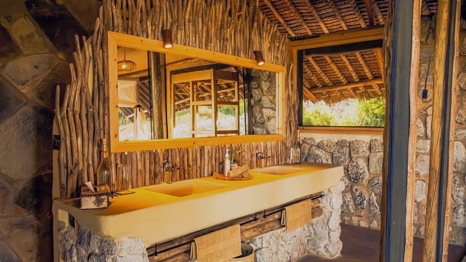 Bathroom at Soroi Cheetah Tented Camp with a basin set in stone, a wide mirror and walls of rough wooden poles