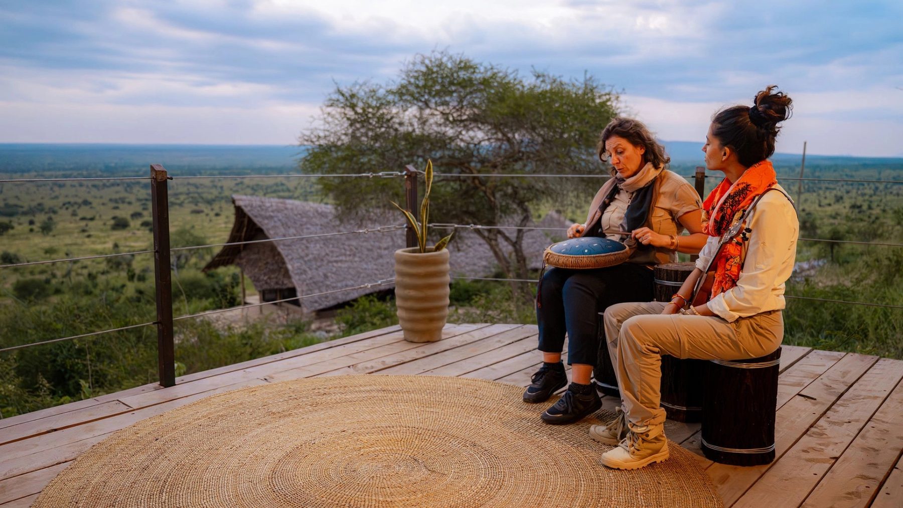 Two guests sitting on a wooden deck at Soroi Cheetah Tented Camp, overlooking thatched roofs and bushland