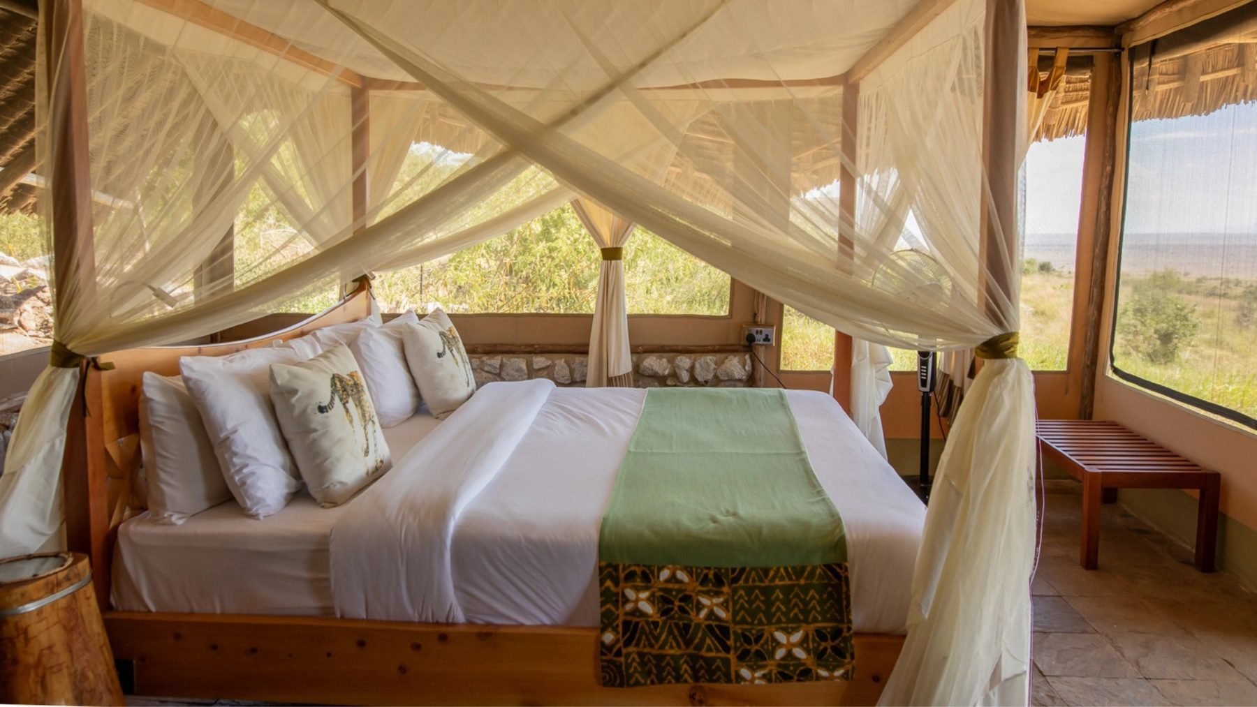 Tent at Soroi Cheetah Tented Camp with a netted four-poster bed, cheetah-print cushions and windows onto the plains