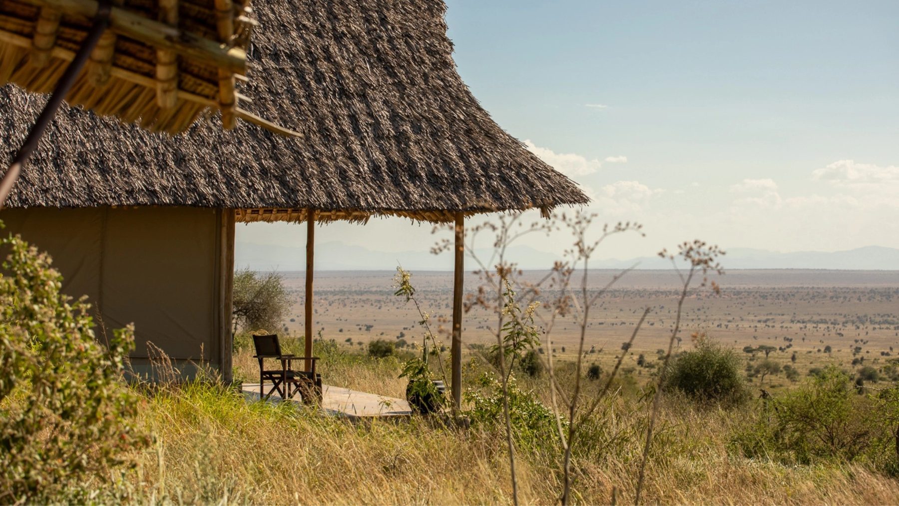 Thatched tent with a chair on its deck at Soroi Cheetah Tented Camp, looking out over wide plains