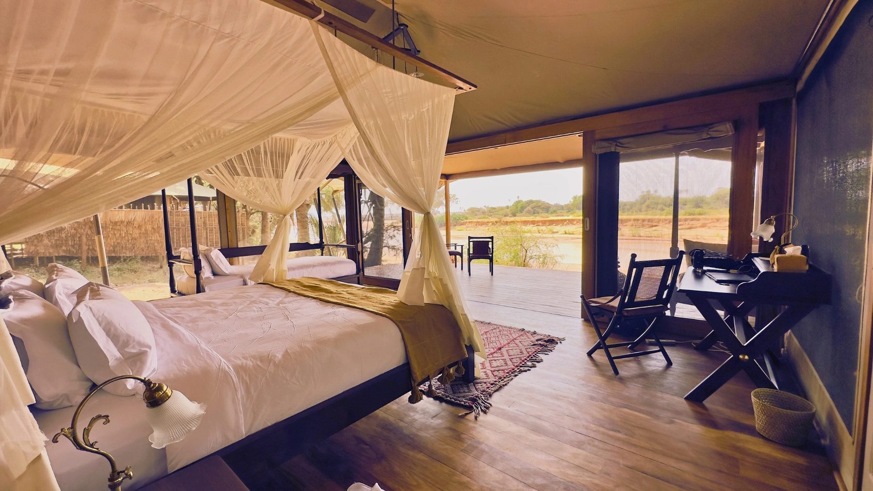 Tent at Soroi Larsens Camp with a netted bed, wooden floor and a desk, its open front looking out to the river