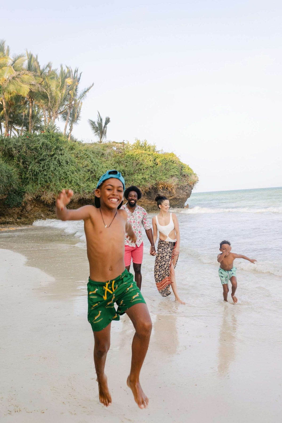 Children running and leaping along the white sand beach in front of Swahili Beach Resort in Diani