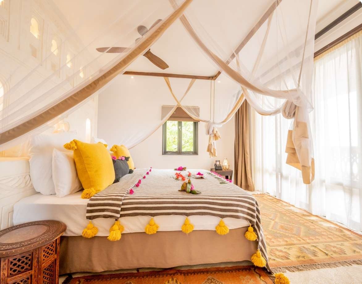 Bed with yellow tasselled cushions and a striped throw under white netting at Swahili Beach Resort