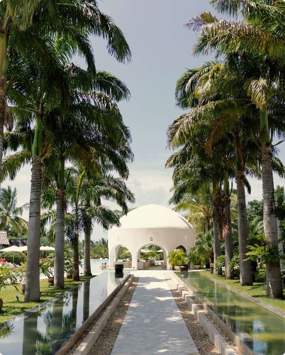 Walkway lined with tall palms and water channels leading to a white domed pavilion at Swahili Beach Resort