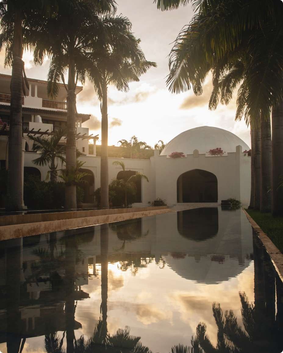 Long reflecting pool between white domed buildings and palm trees at Swahili Beach Resort at sunset