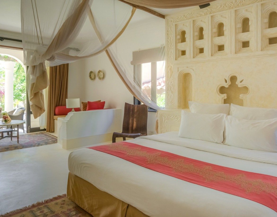 Bedroom at Swahili Beach Resort with a wide bed, a red runner, carved plaster niches and draped netting