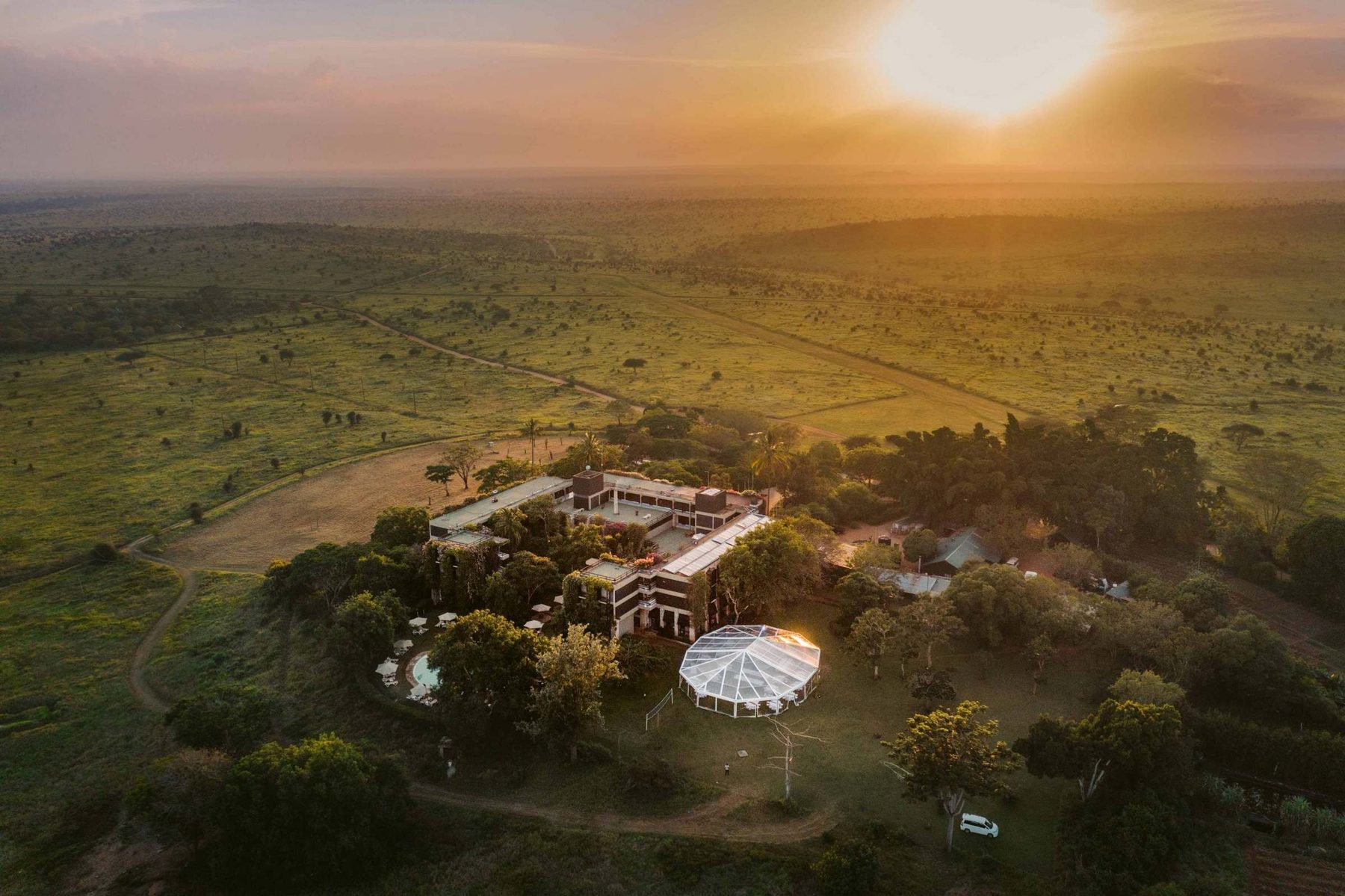 Aerial view of Taita Hills Safari Resort & Spa among trees on green grassland as the sun rises