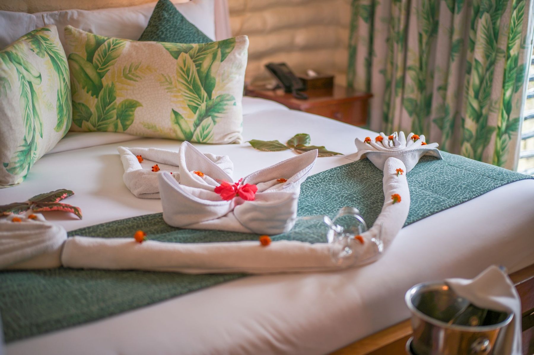 Folded towels and petals on a bed with leaf-print cushions at Taita Hills Safari Resort & Spa