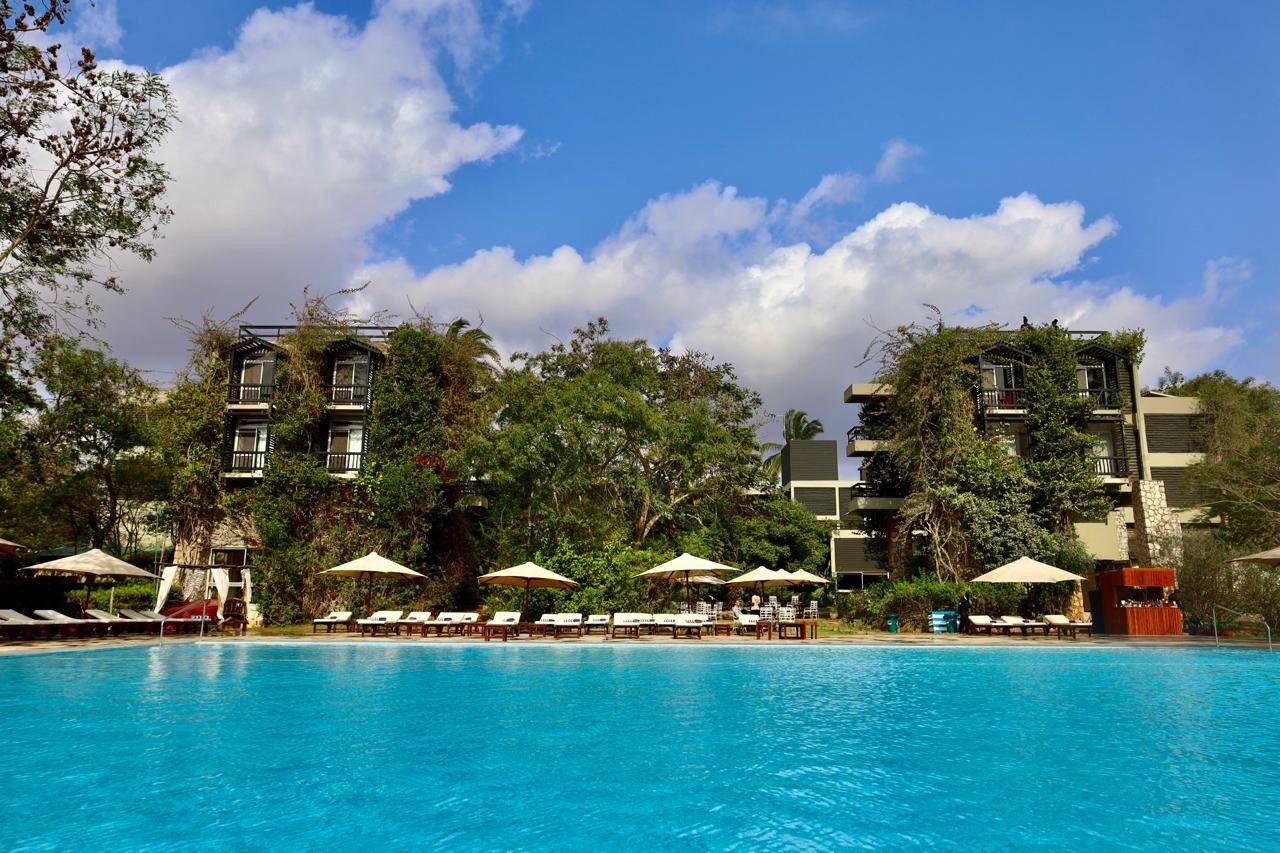 Large blue pool lined with umbrellas and loungers below ivy-covered buildings at Taita Hills Safari Resort & Spa