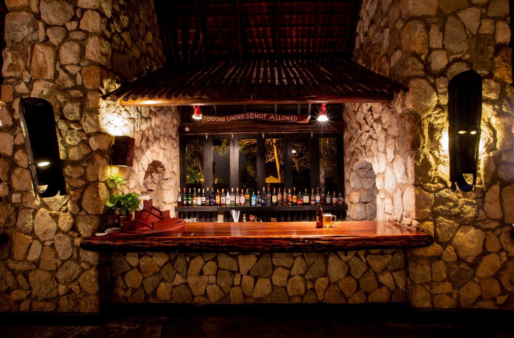 Lit bar counter set into stone walls with shelves of bottles at Taita Hills Safari Resort & Spa