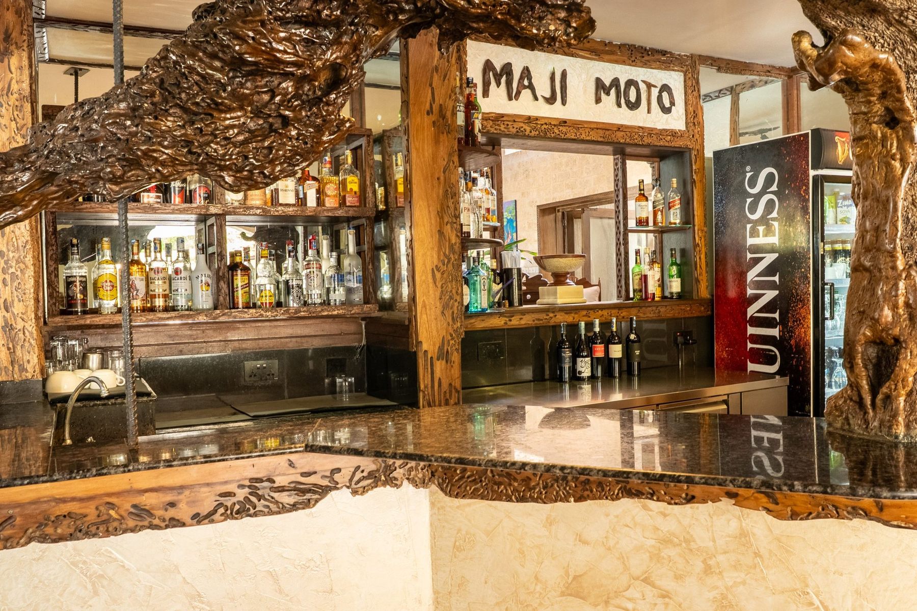 The Maji Moto bar at The Maji, with a carved driftwood frame and shelves of bottles