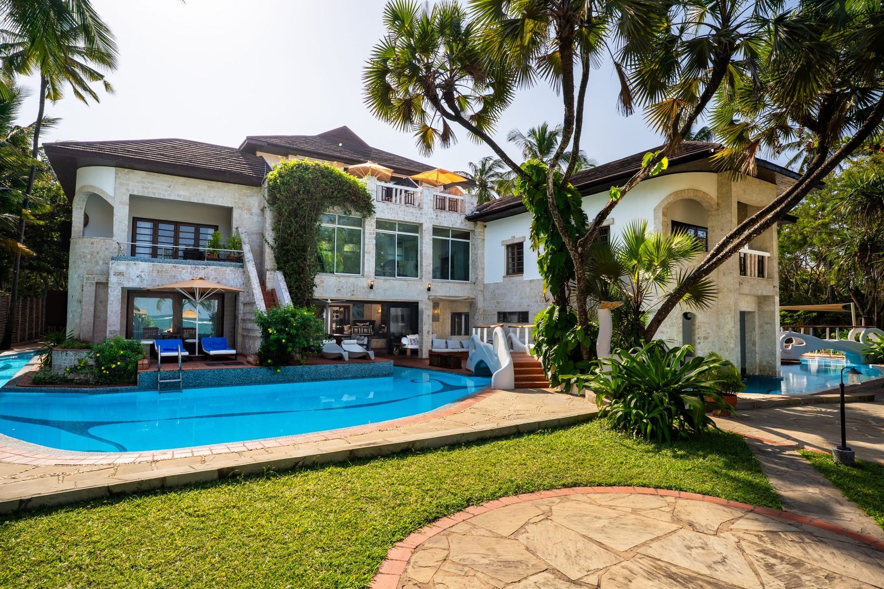 The Maji’s pool and lawn in front of the white, three-storey main house among palms