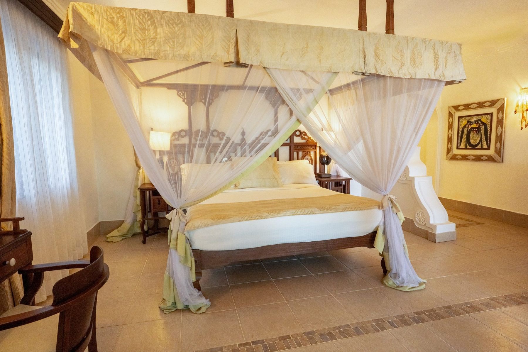 Garden suite at The Maji with a carved four-poster bed draped in netting
